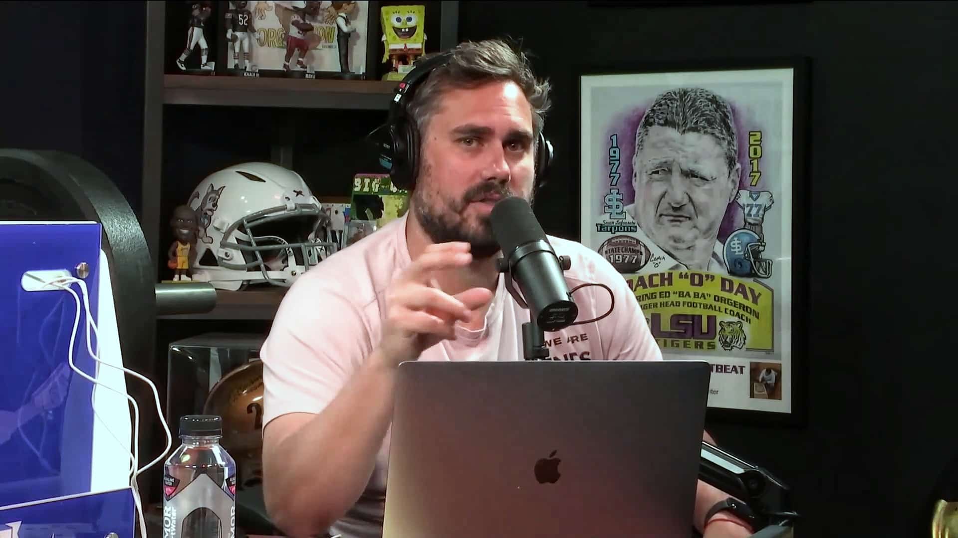 Man wearing headphones speaking into a microphone while recording a podcast at a desk with a laptop